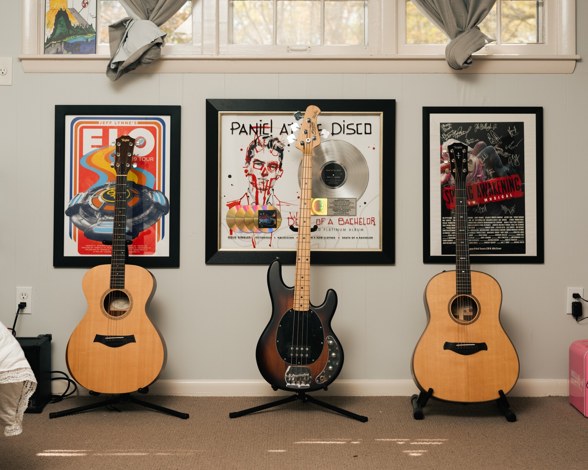 A Panic at the Disco and "Spring Awakening" poster are framed on a wall near three guitars.