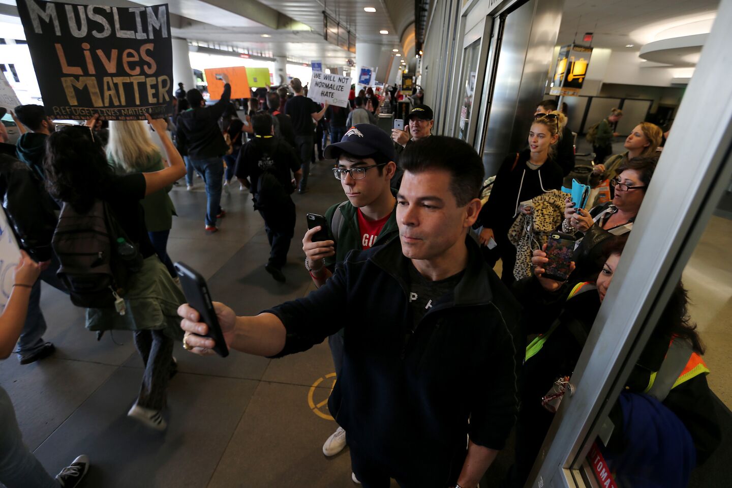 Passengers stand in the doorway of a baggage claim area to take pictures and video of marchers protesting the immigration ban of President Trump at LAX on Saturday.