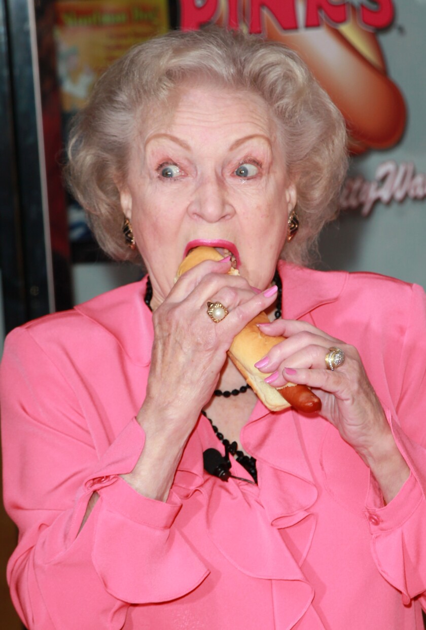 A woman in a pink blouse biting into a hot dog