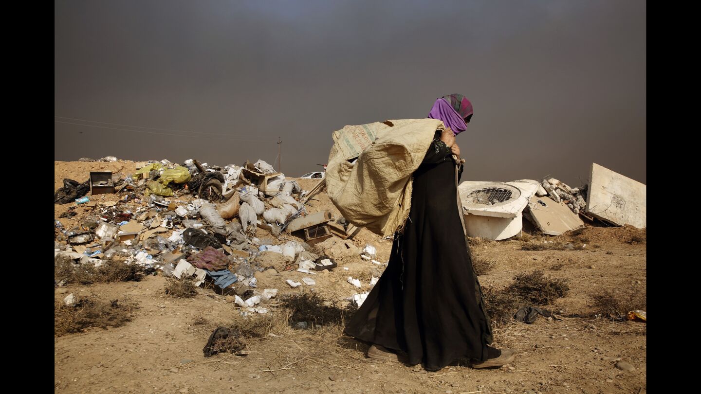 A woman rummages through garbage under smoke-filled skies in the town of Qayyarah. The residents of Qayyarah were liberated from Islamic State forces, but left with destruction and contamination from burning oil wells.