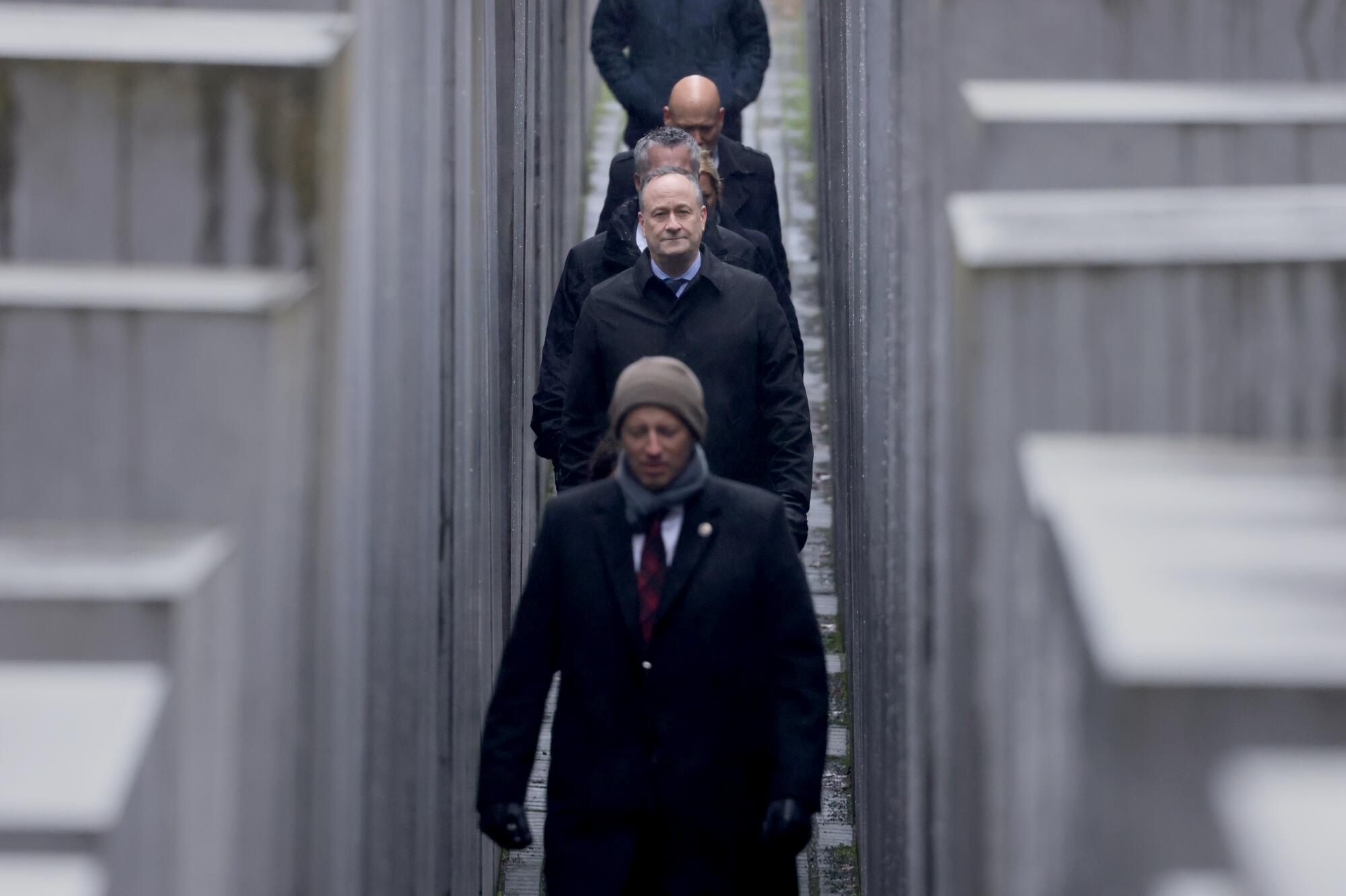 Douglas Emhoff, flanked by security, walks among concrete blocks of a memorial
