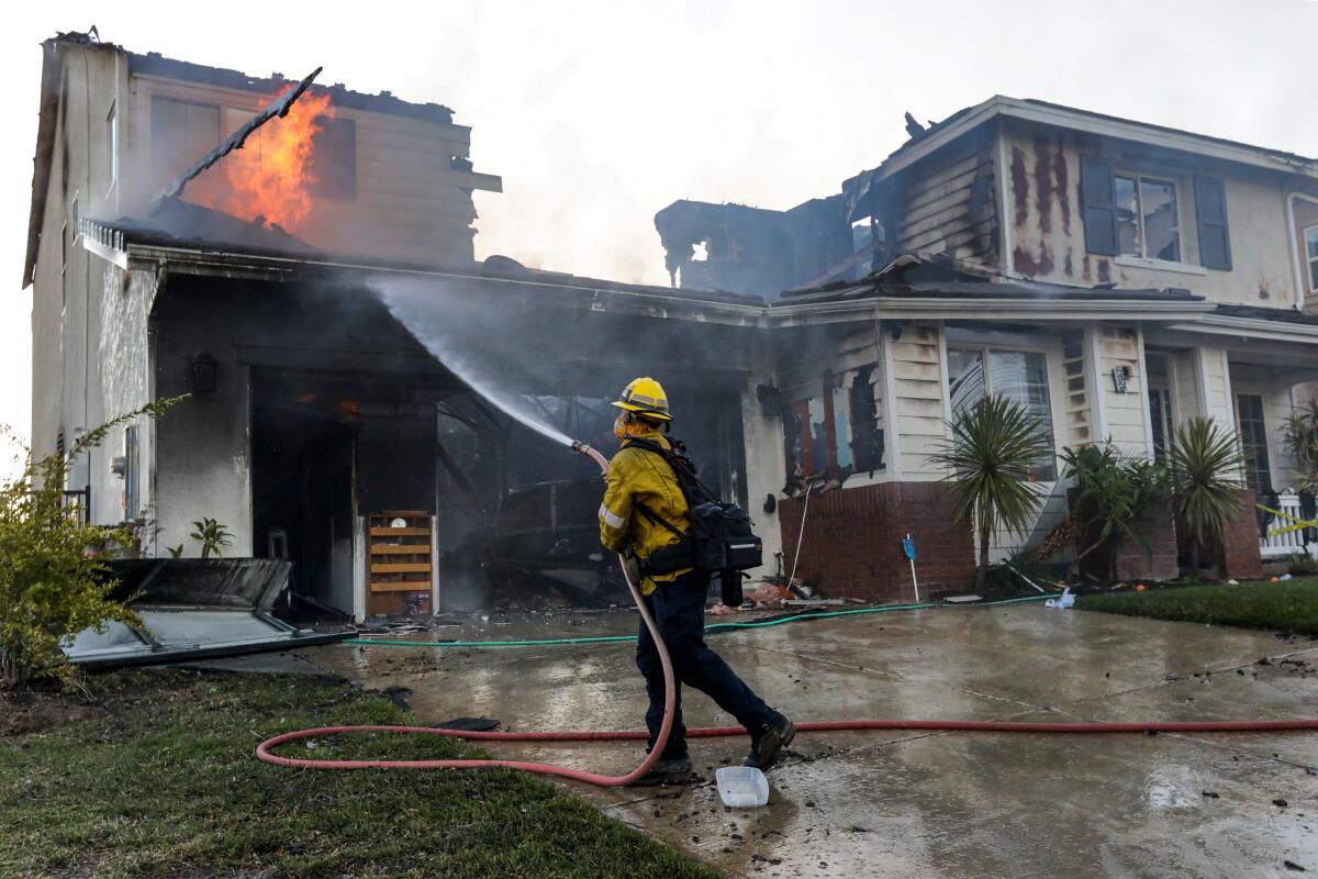 A firefighter hoses down a house in the 29000 block of Sequoia Road in Santa Clarita on Friday. The Tick fire has destroyed at least six homes and damaged an unknown number of others since it broke out Thursday