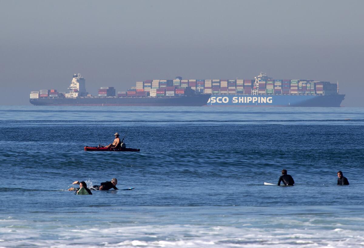 Surfers float in the foreground as a large cargo ship floats in the distance.