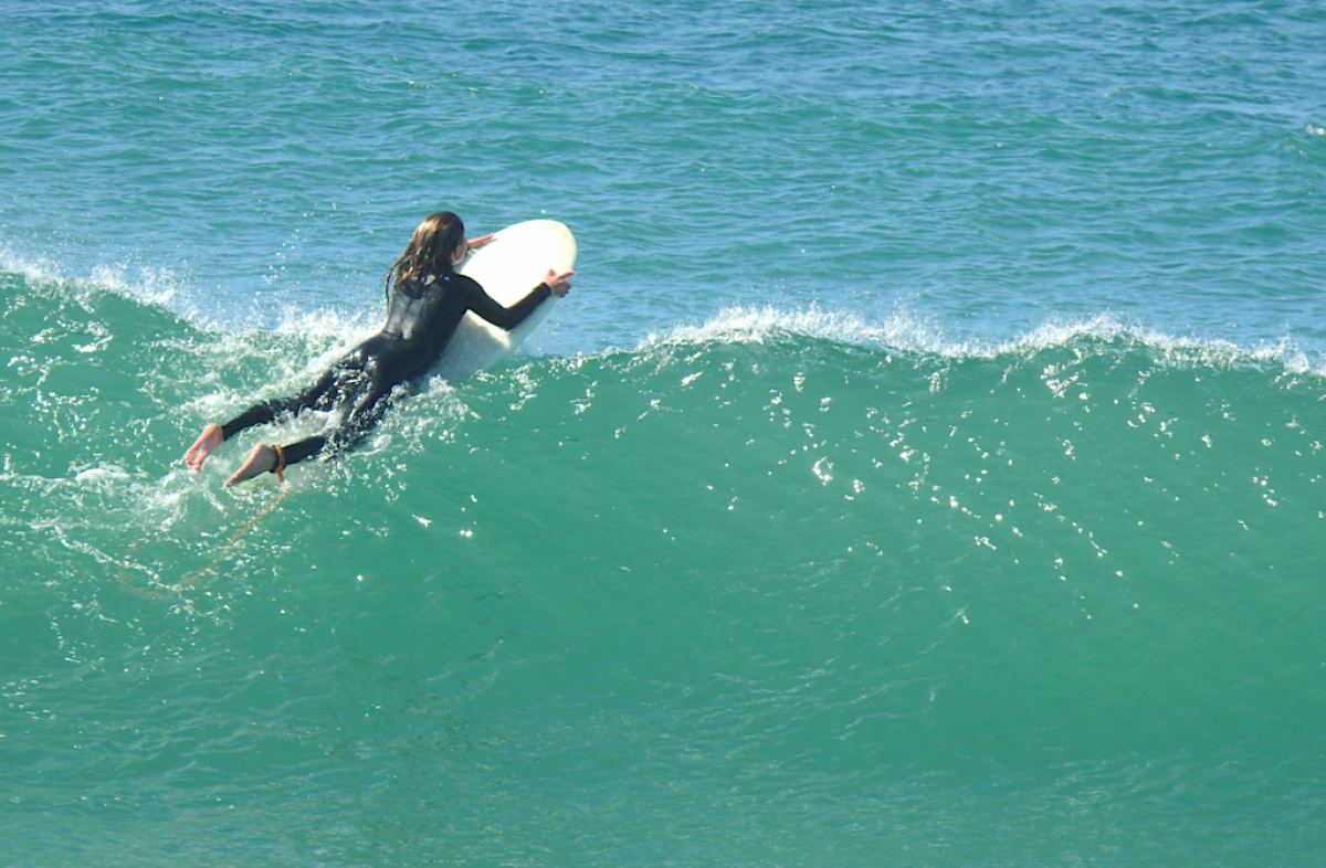 Una niña flota sobre una ola encima de una tabla de surf