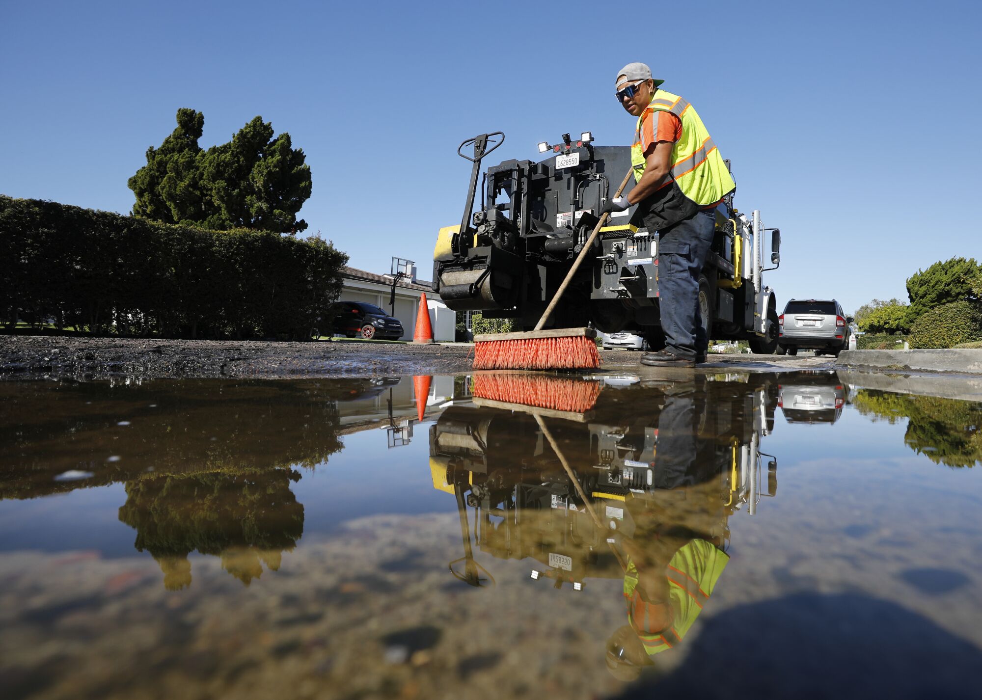 Anthony Ortega with the City of San Diego clears water out of pothole to prepare it for repair 