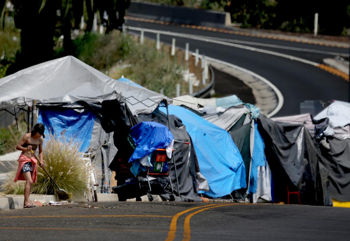 A homeless woman sweeps up 8th Street near an encampment along the Harbor Freeway in Los Angeles.