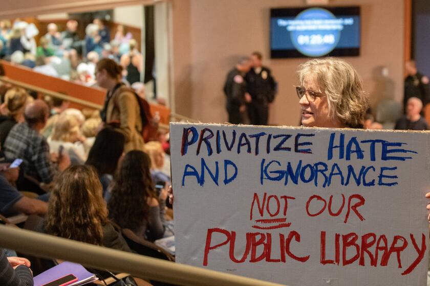 A woman who came out in support of an item that would require voters to decide whether Huntington Beach's libraries would be privatized holds a sign, while searching for a seat in a packed audience section overlooking the chamber floor.
