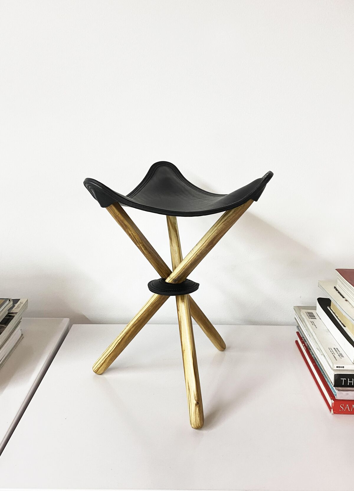 A three-legged stool with wooden legs and a leather seat.