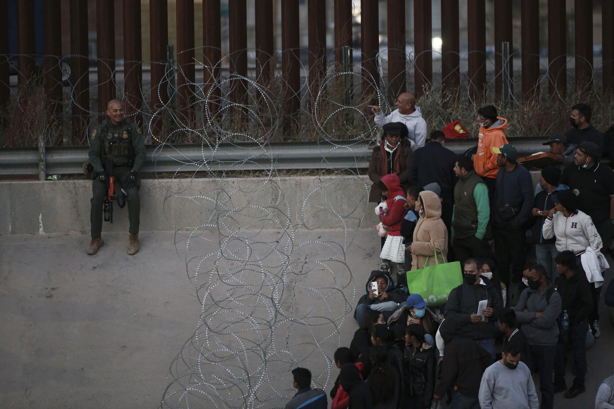 Migrants stand behind barbed wire as a barrier from crossing into El Paso, Texas