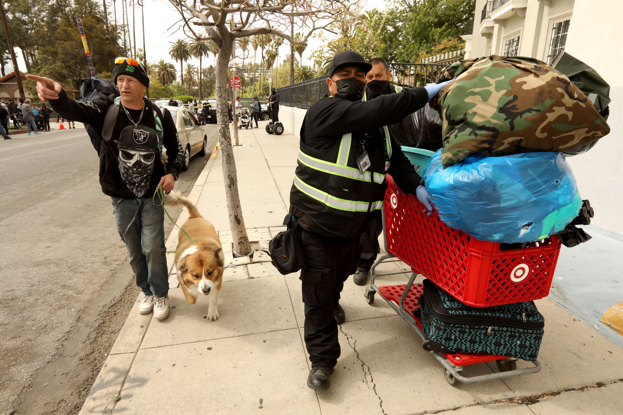Two men push a shopping cart with a homeless man's belongings.