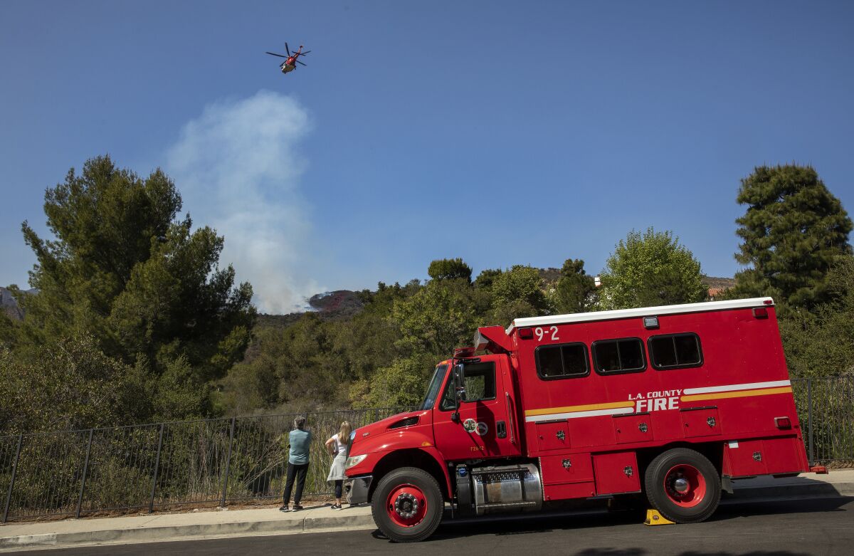 A helicopter prepares to drop water on the brush fire in Pacific Palisades