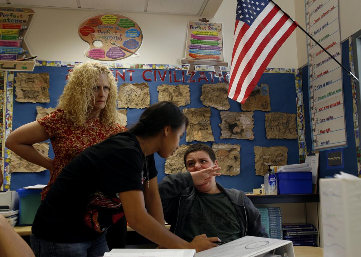 Behavior specialist Michelle May tries to calm down 13-year-old Jonah Funk after he starts biting his hand while working with Sarabeth Rothfeld, in back, at Hesby Oaks School in Encino.