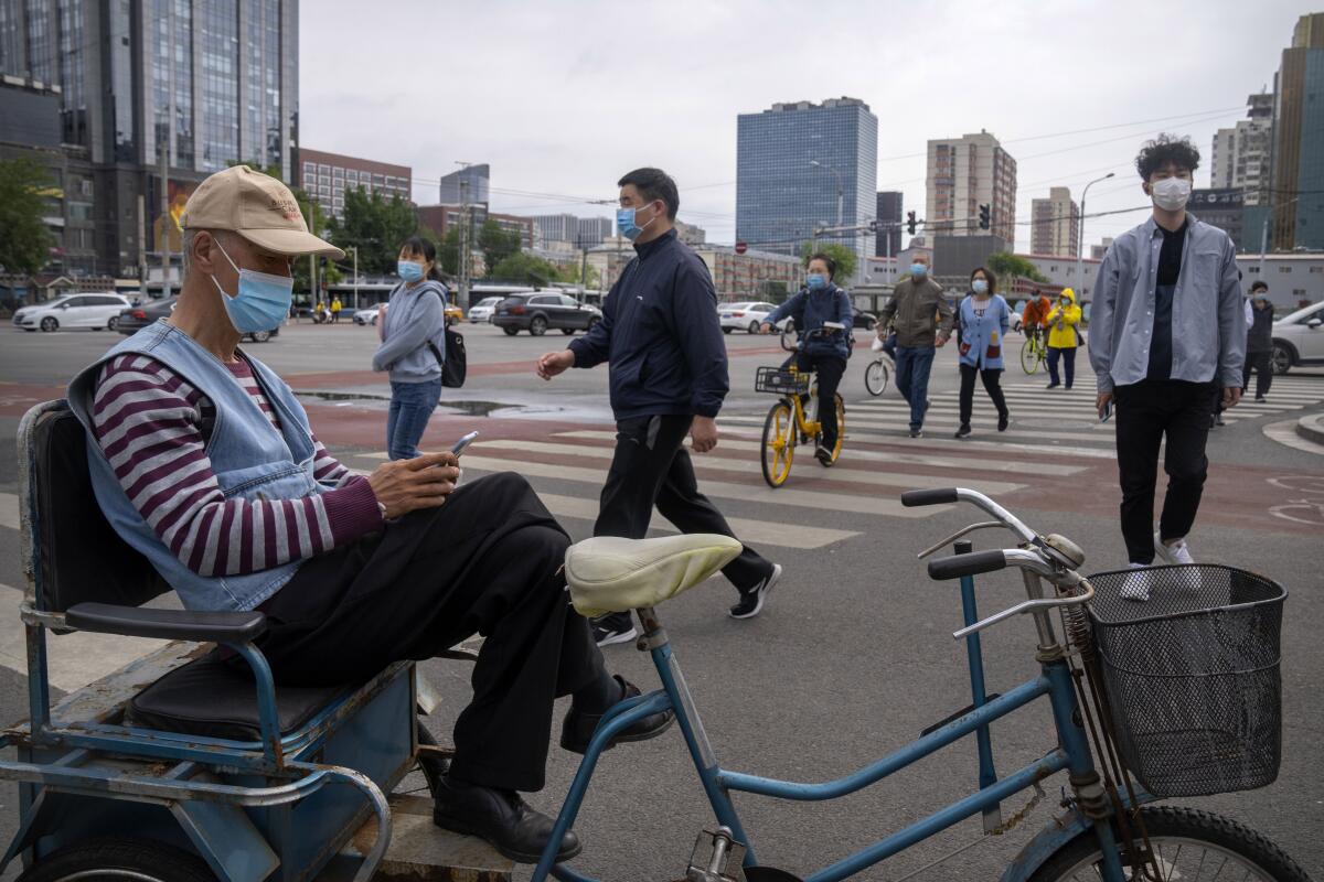Un hombre sentado en su bicicleta mientras otros caminan en una intersección en Beijing