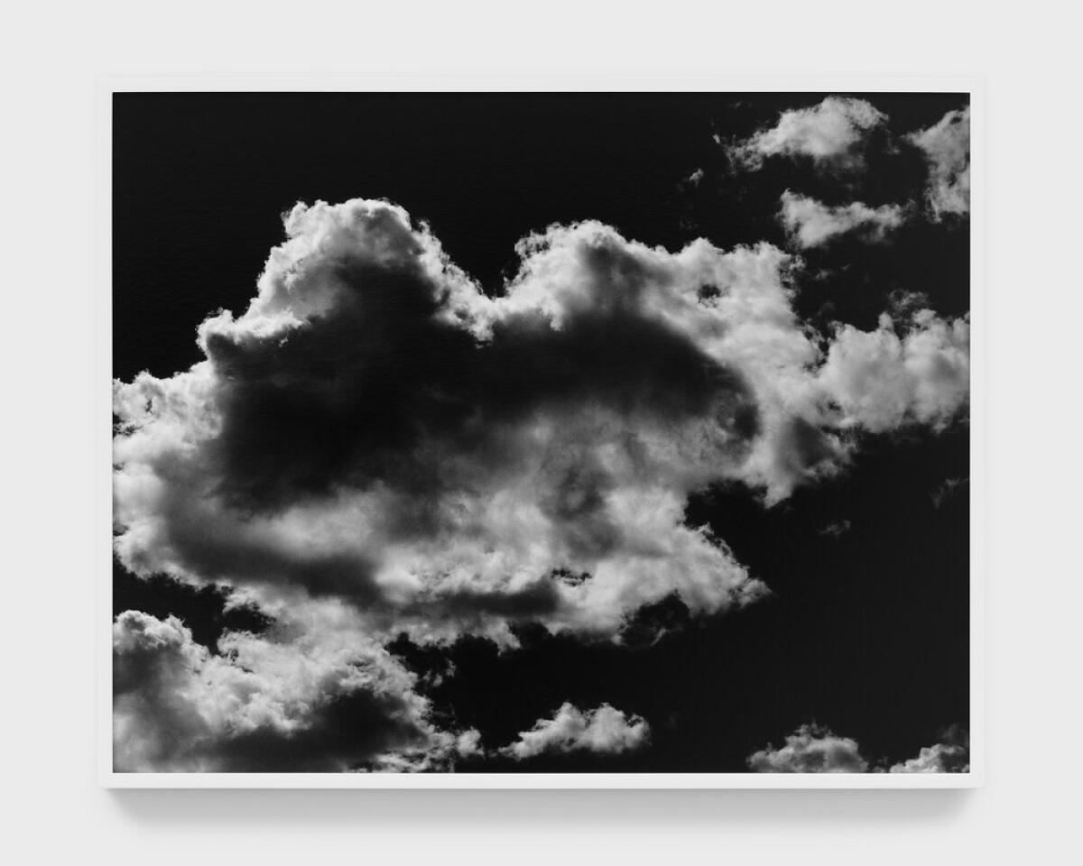 A black and white photograph hanging on a gallery wall shows an image of white clouds amid a darkened sky
