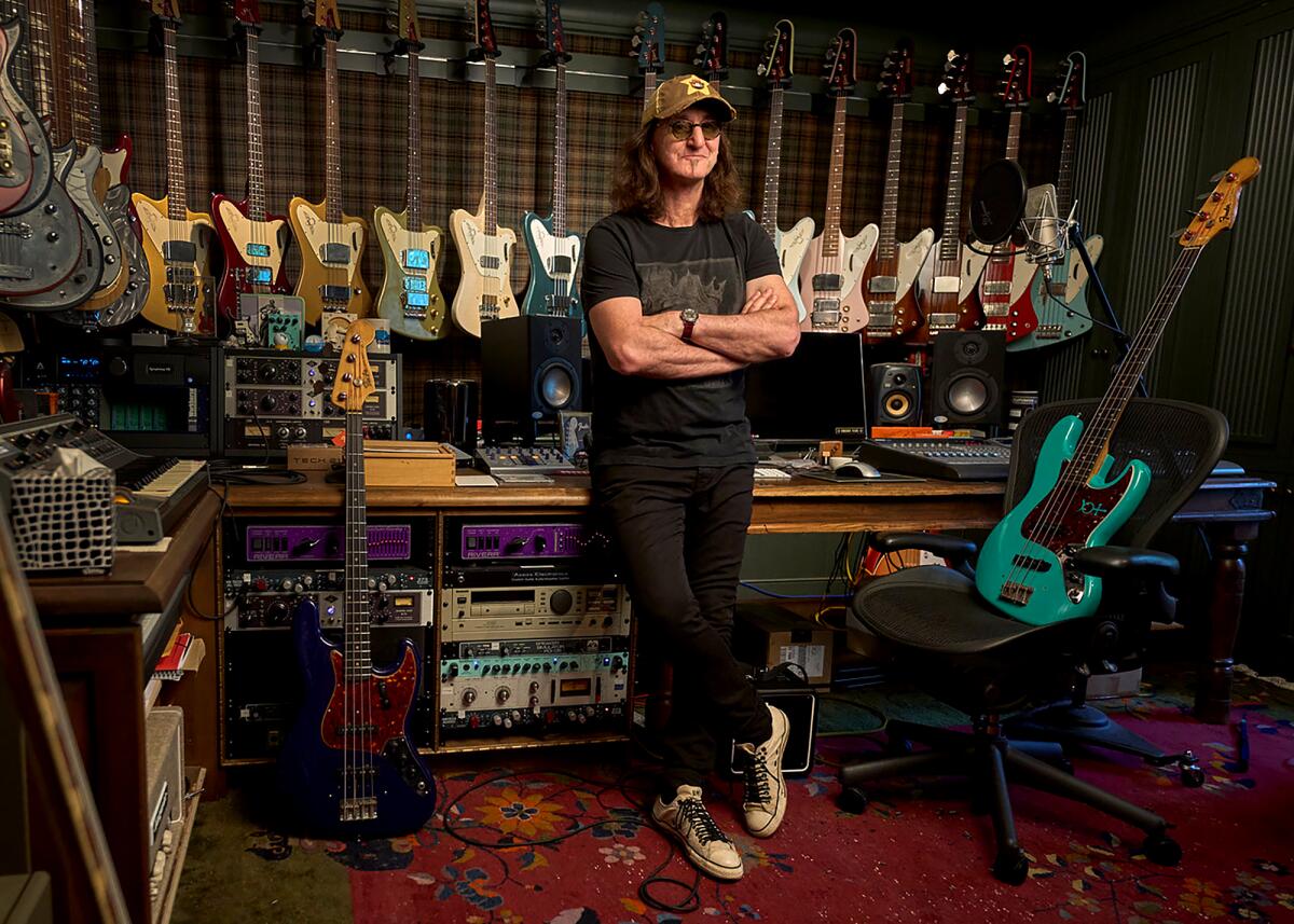 Geddy Lee in front of a wall of guitars