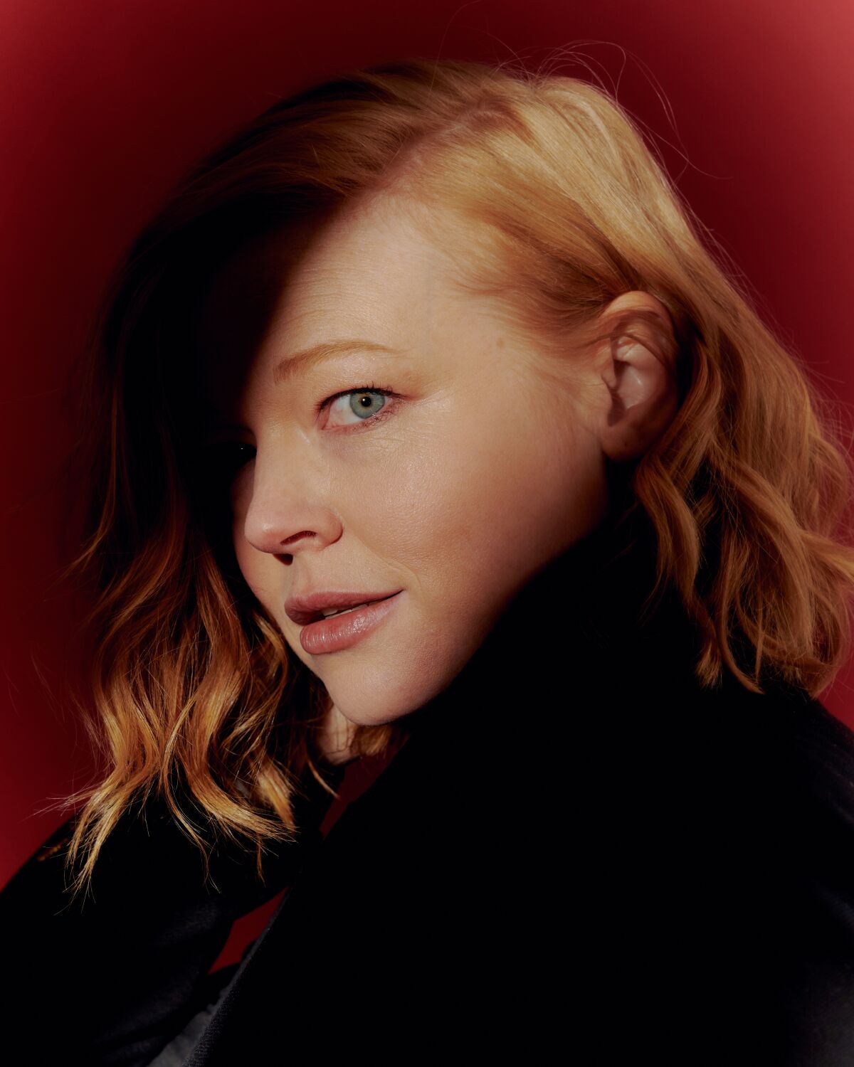 From the shadows a light shines on the left side of Sarah Snook's face.