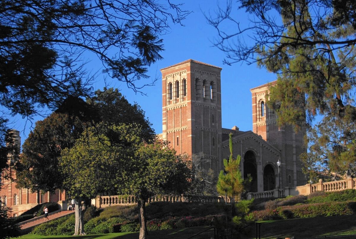 The towers of Royce Hall rise against a blue sky, with trees in the foreground.