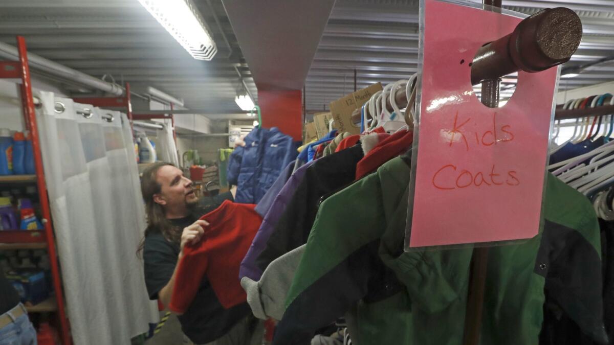 Brent Dalton, day shift supervisor at the Road Home shelter, hangs up donated children's coats in the warehouse.