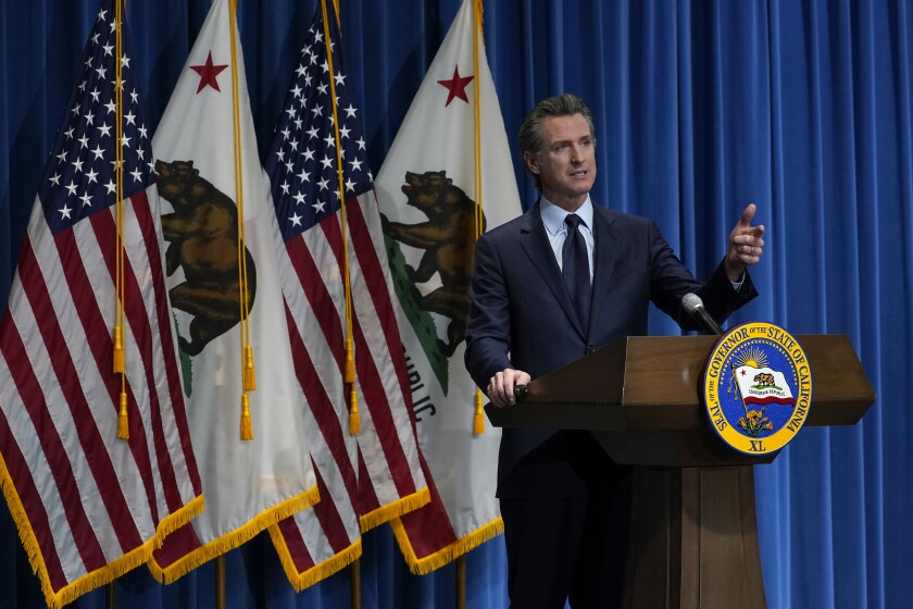 Governor Gavin Newsom speaks at a lectern in front of U.S. and California flags
