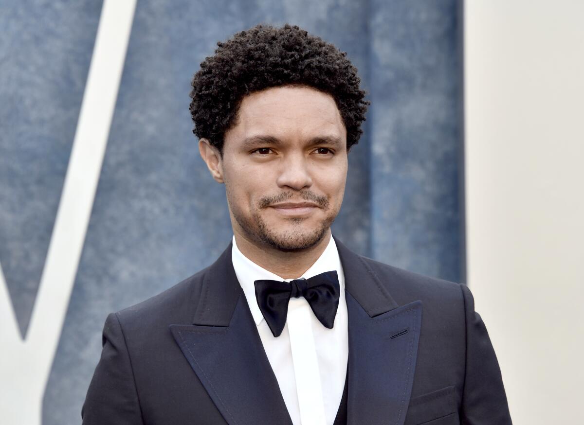 Trevor Noah giving a slight grin while wearing a dark blue tuxedo with a black bow tie 