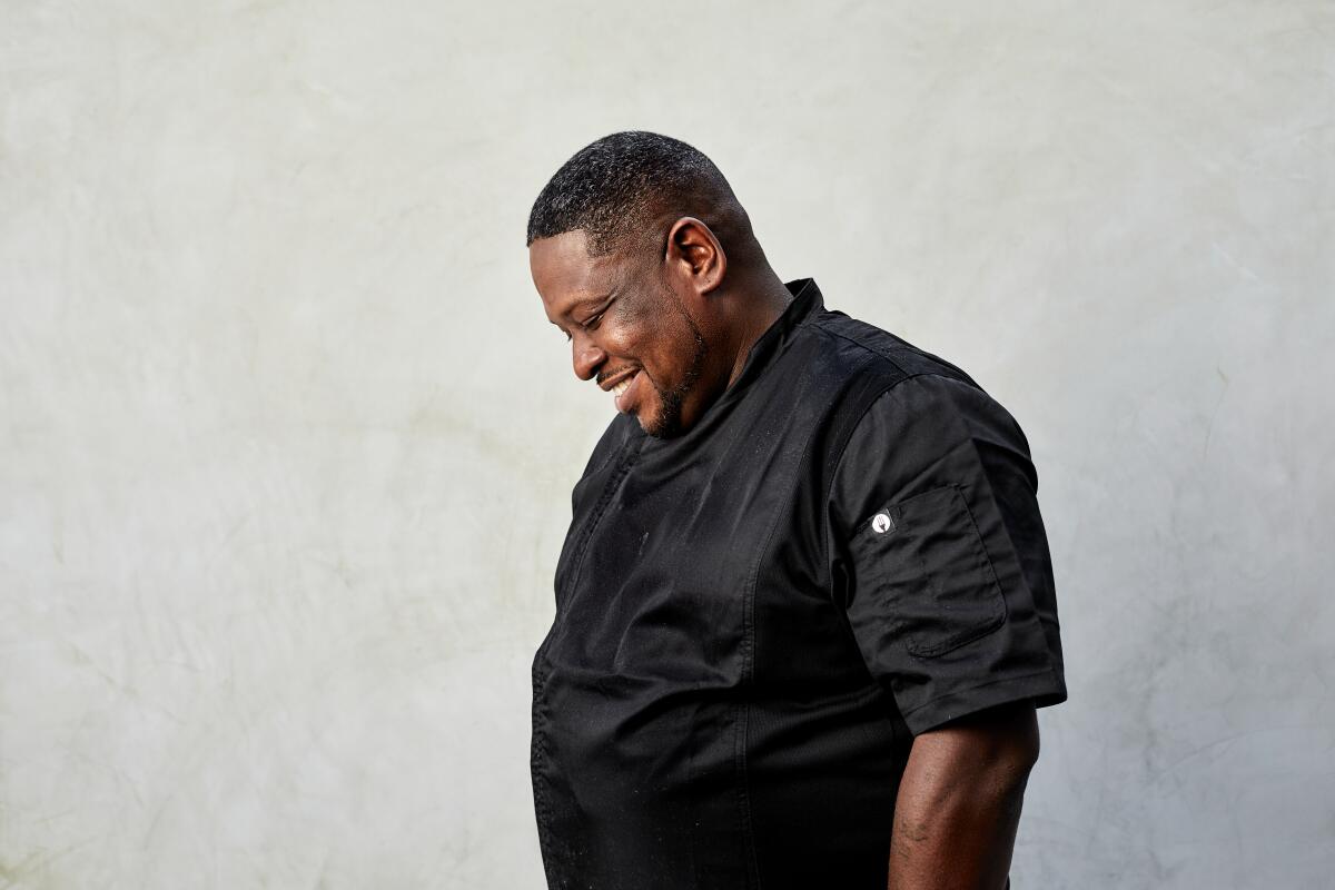 A man in a black shirt smiles and looks down