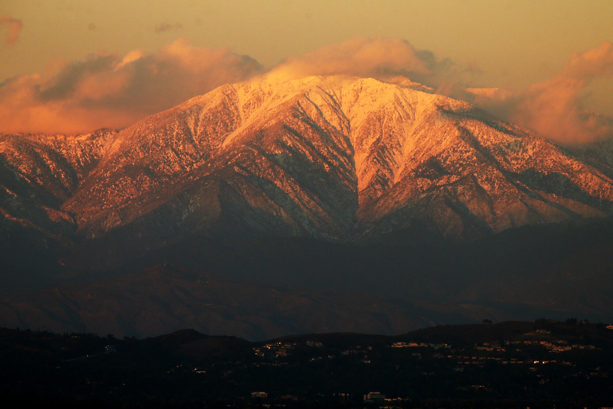 The setting sun casts a golden glow on the snow-covered peaks of Mt. Baldy.