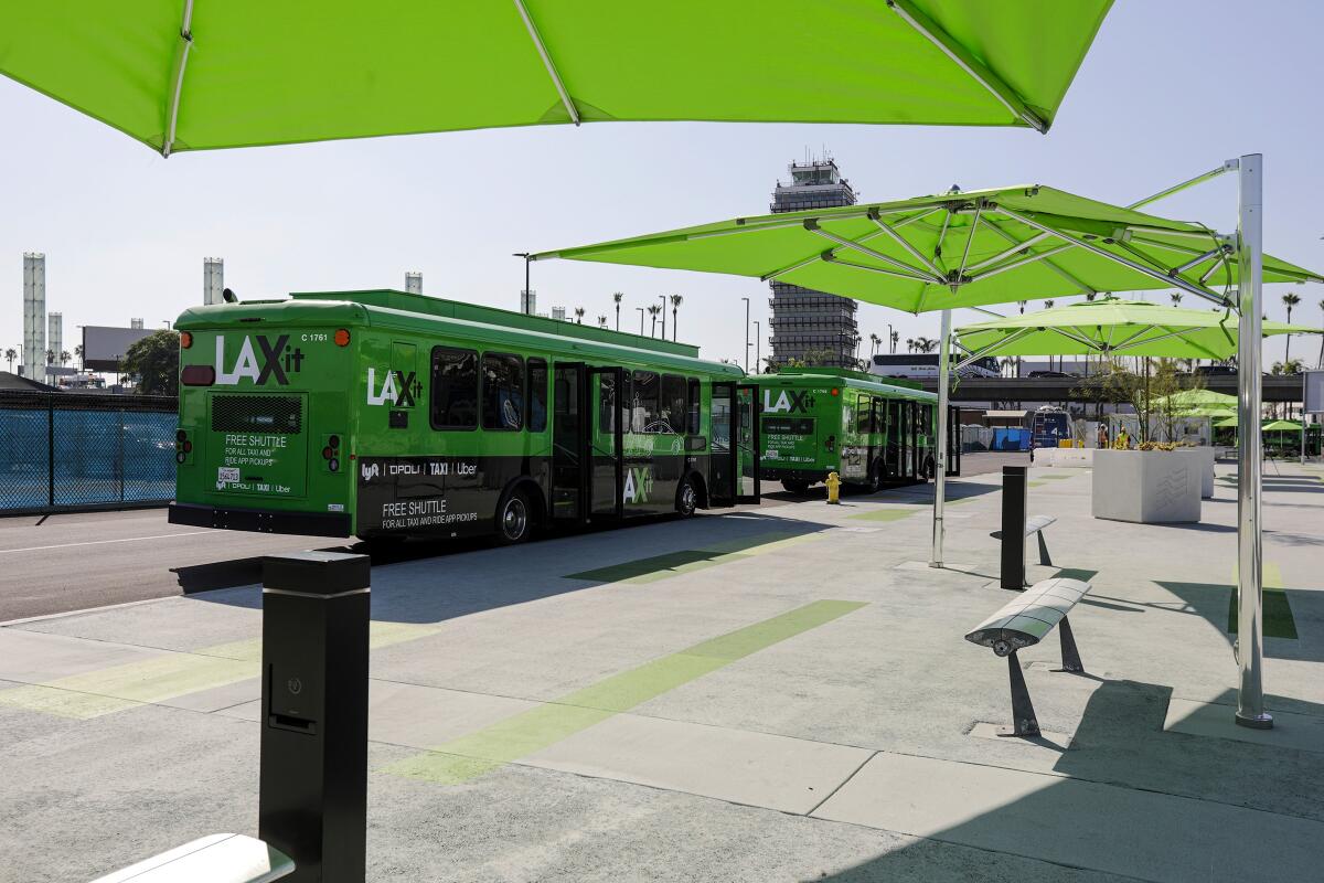 The LAX-it pickup lot with green and black buses and green umbrella-style coverings over benches.