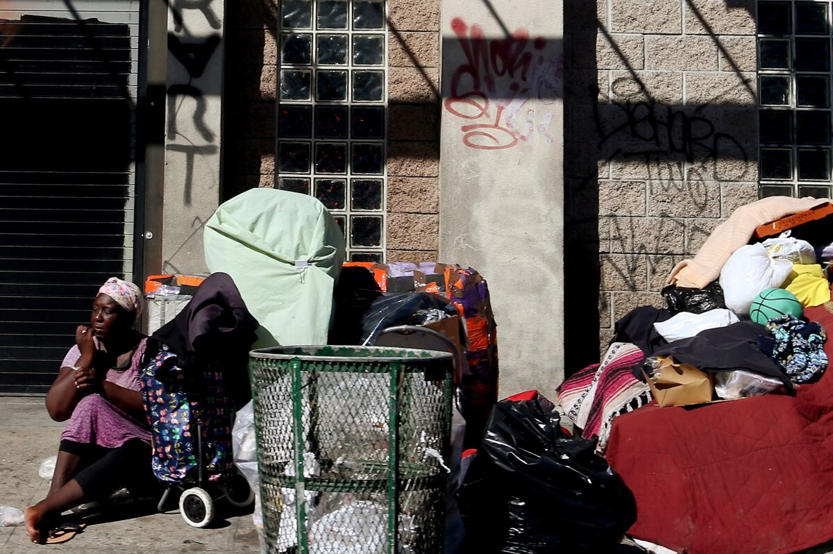 A woman sits beside her belongings on the sidewalk along 6th Street in Los Angeles.