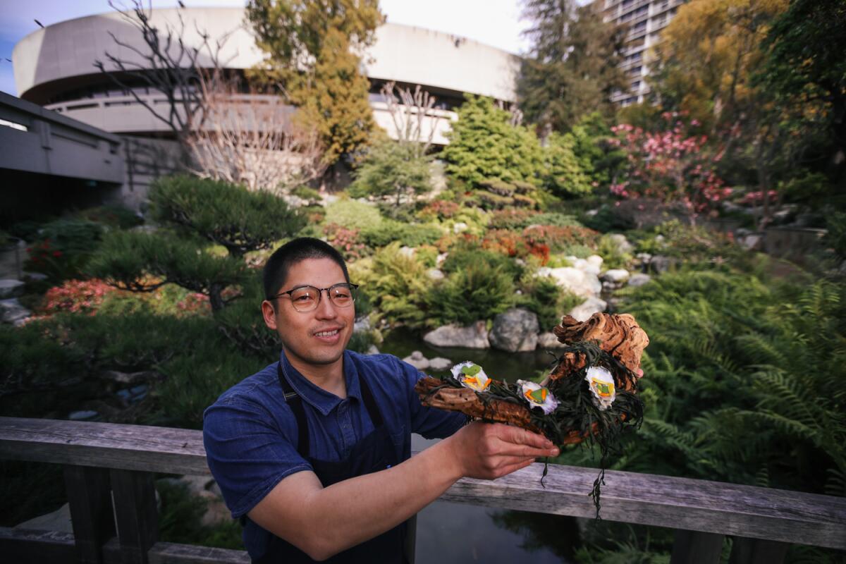 Chef Chris Ono displays a dish standing in the garden of a museum