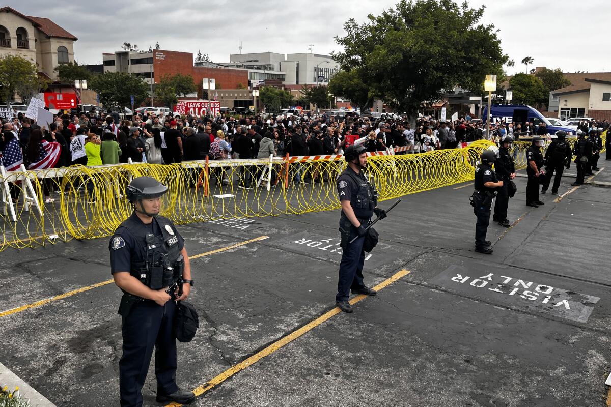 Police officers stand in a line in front of a barrier keeping a crowd back 