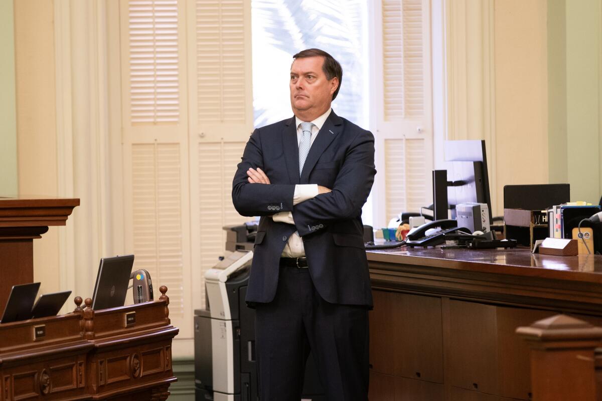 Former Assemblyman William Brough stands, arms folded, in front of a desk