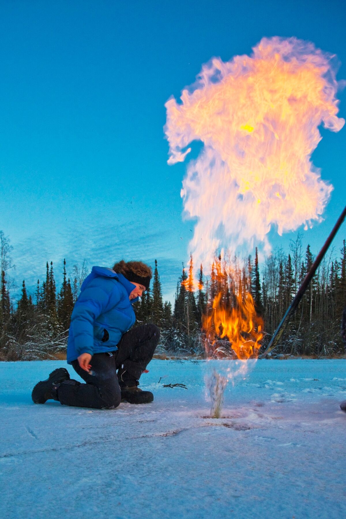A woman kneels on a frozen lake with a plume of flame in front of her