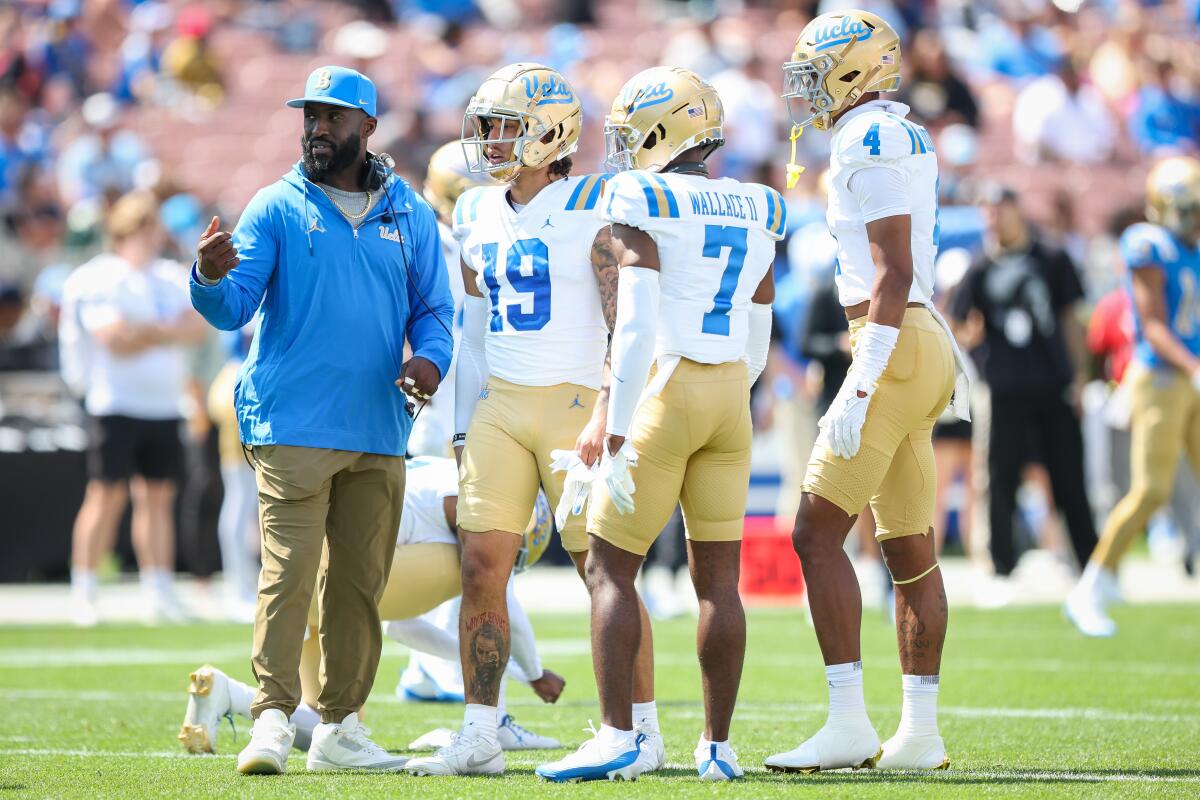UCLA coach DeShaun Foster talks with defensive back DJ Justice (19), K.J. Wallace II (7) and Bryan Addison (4).