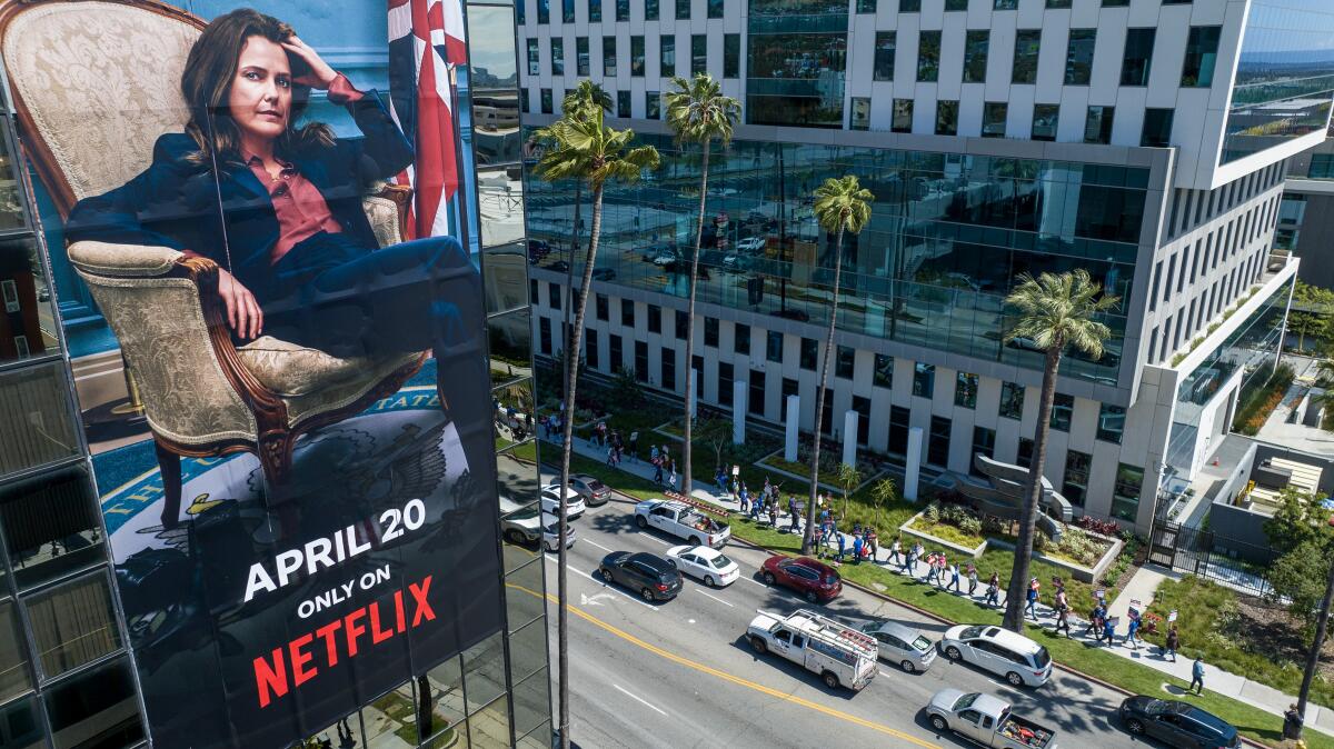 A billboard for a Netflix show looms over a picket line in front of a studio used by Netflix.