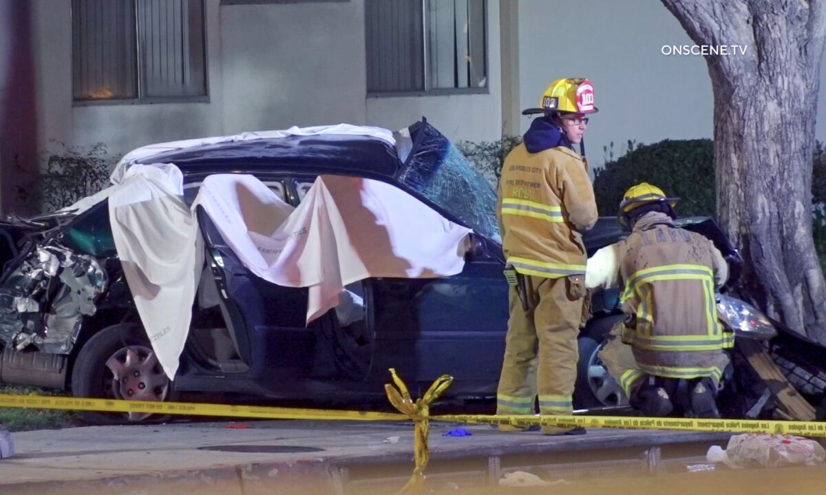 Firefighters outside a crashed sedan with white sheets draped over the wreckage