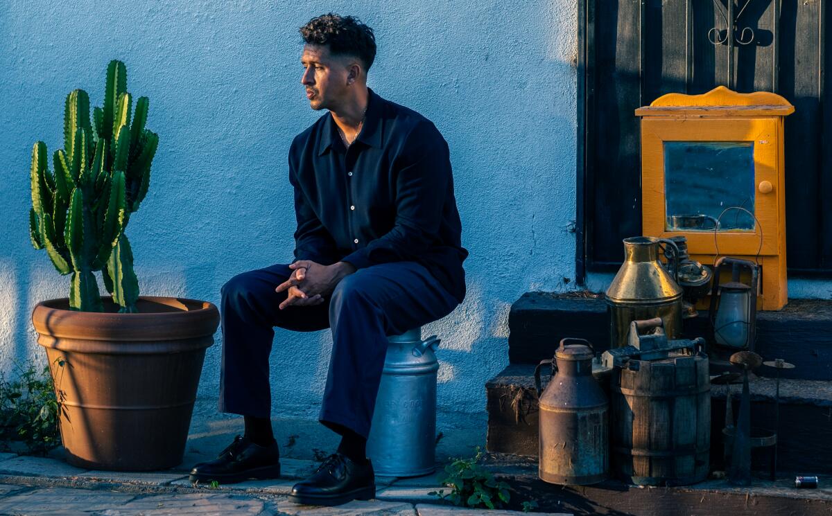 A man sits in front of a blue wall, next to a potted cactus