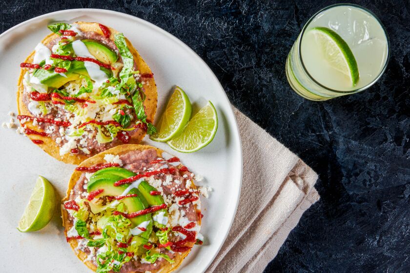 Two bean and cheese tostadas drizzled with hot sauce and crema and limes on the side. 