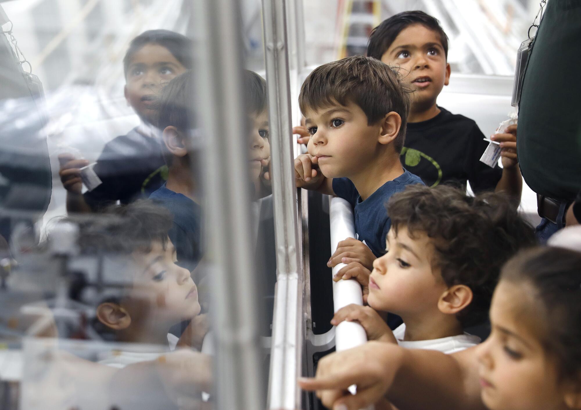 Children look through a window into the clean room where JPL where the Europa Clipper spacecraft is assembled.