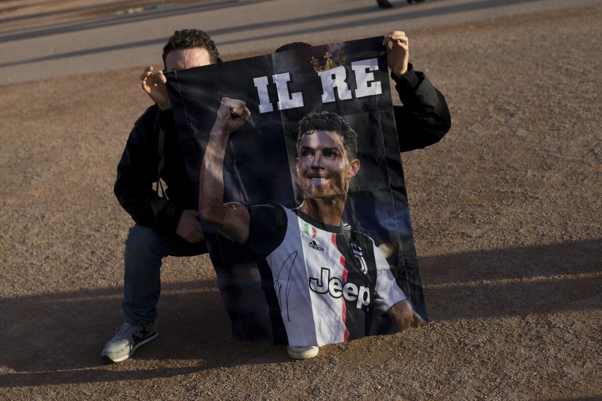 Juventus supporters display a flag depicting Cristiano Ronaldo during a visit to Lyon, central France, ahead of the Champions League , round of 16th, first leg match Lyon against Juventus, Wednesday Feb. 26, 2020. Up to 3,000 Juventus fans are expected. As the coronavirus cases clustered in northern Italy kept climbing and European countries reported new ones with Italian travel ties Tuesday, authorities across the continent tried to strike a balance between taking prudent public health measures and preventing panic. (AP Photo/Daniel Cole)