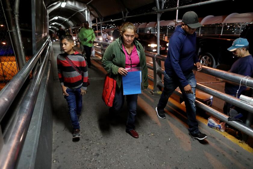 CIUDAD JUAREZ, CHIHUAHUA -- THURSDAY, SEPTEMBER 26, 2019: Dilcia Sabillon Aceituno, 40, of Naco, Honduras, with her twin son Anthony Leiva Sabillon, 12, cross the Paso del Norte international port of entry bridge around 4:30 a.m. for their asylum hearing in El Paso, in Ciudad Juarez, Chihuahua, on Sept. 26, 2019. Dilcia had to flee Honduras when gangs tried to recruit her twin sons to distribute drugs. Sabillon was returned to Ciudad Juarez under "Remain in Mexico" with one of her twin 12 year-old boys while her husband and the other boy, Nostier Leiva Sabillon, were allowed to stay in the U.S. in Houston. She is staying at the Pan de Vida migrant shelter in Ciudad Juarez. (Gary Coronado / Los Angeles Times)