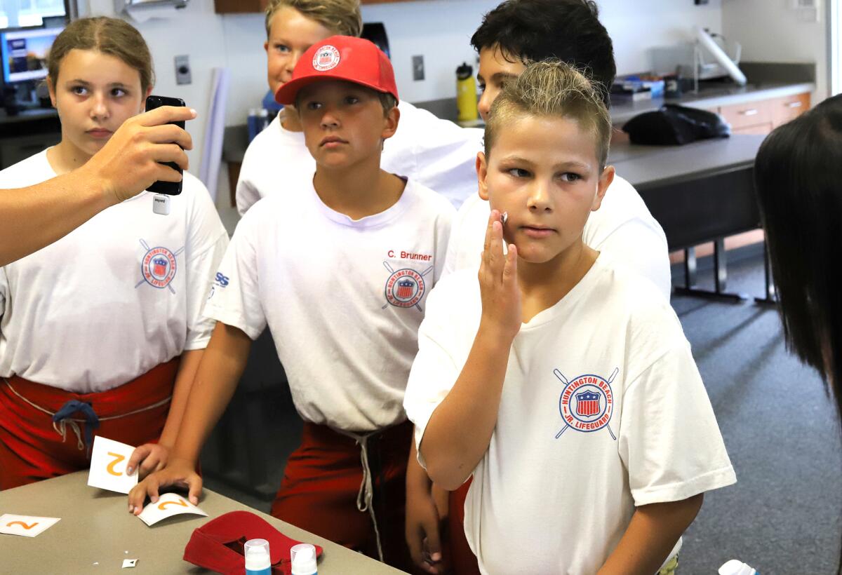Ryder Maragos, 10, right, with other Huntington Beach Junior Lifeguards are shown how to correctly apply sunscreen.
