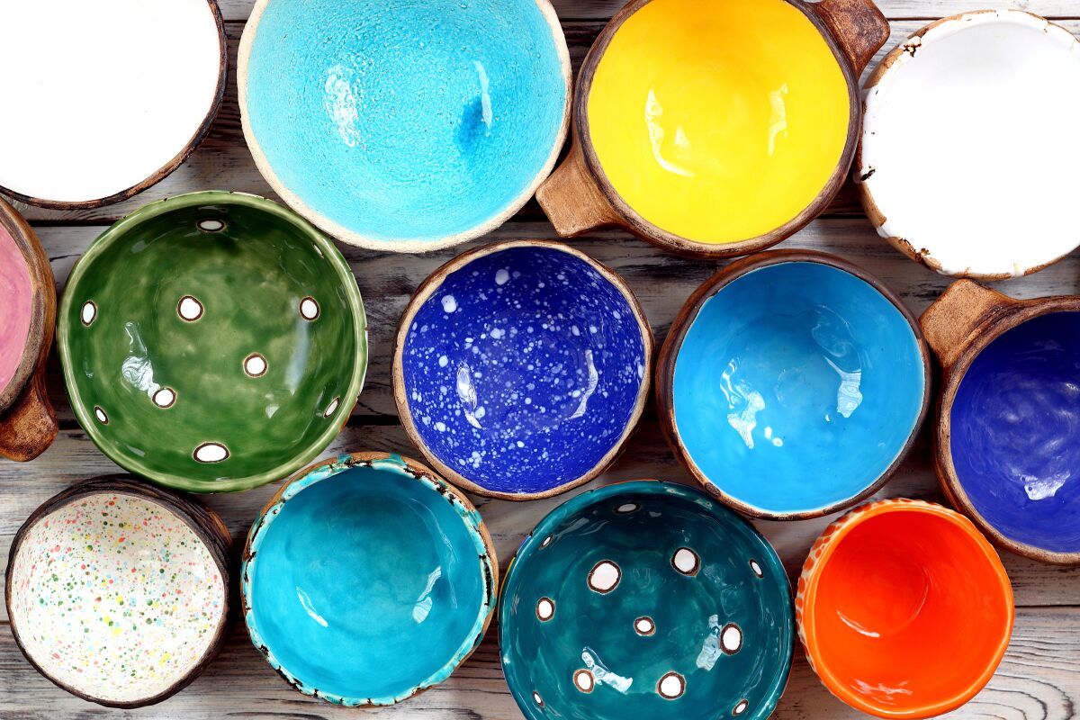 View from above on many different bright multicolored ceramic bowls and cups handcrafted on white wooden background.