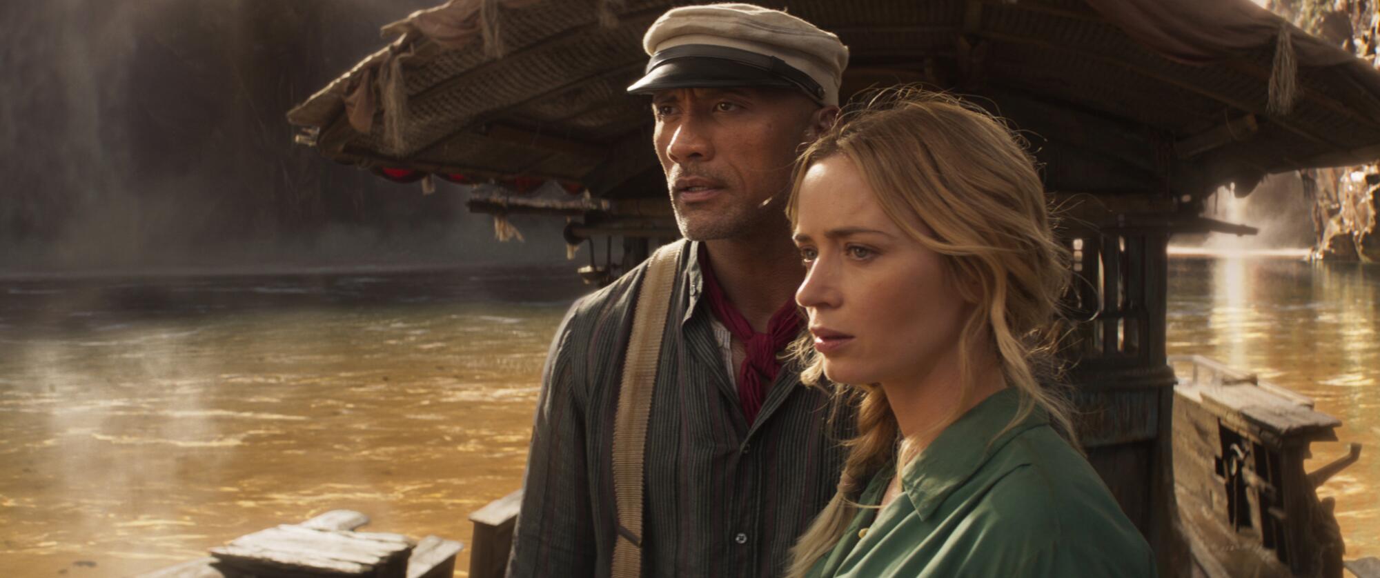 A man in suspenders and a cap, left, and a woman on a boat in a dark river