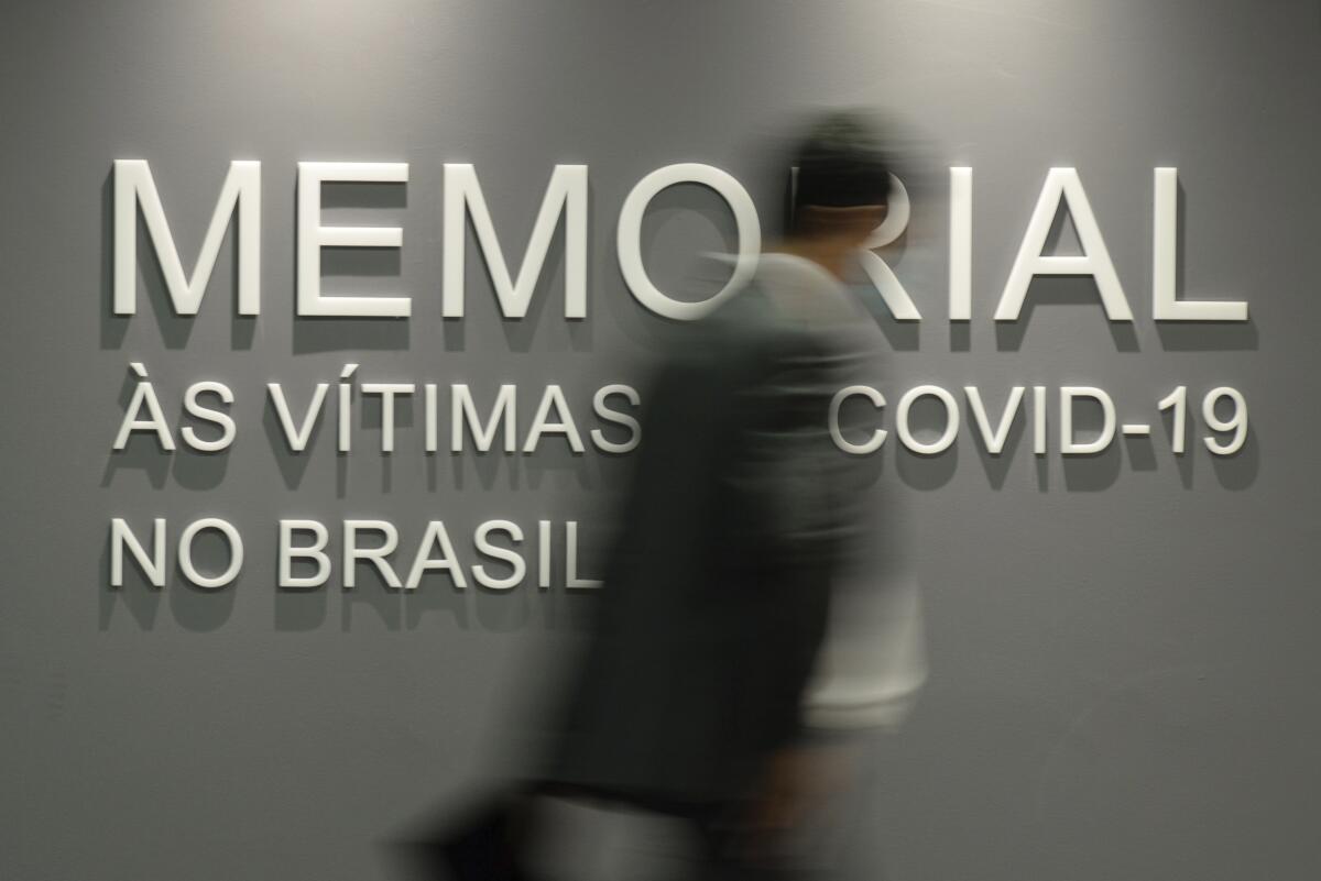A man walks past a wall bearing the words in Portuguese "Memorial to the victims of COVID-19 in Brazil."