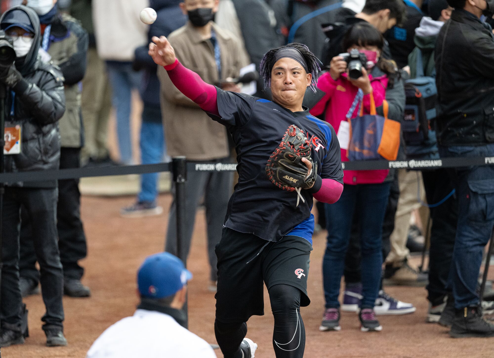 A baseball player in a mostly black uniform throws a ball 