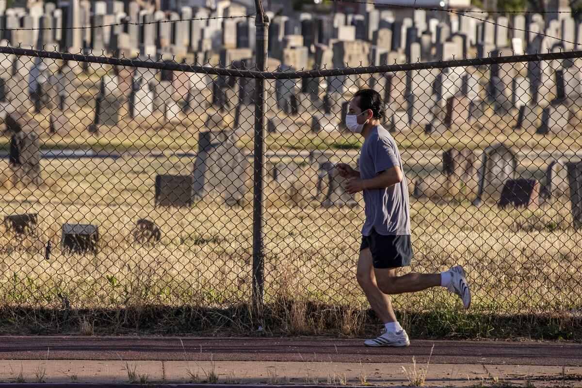 A jogger wearing a mask runs past Evergreen Cemetery in Boyle Heights on Tuesday.