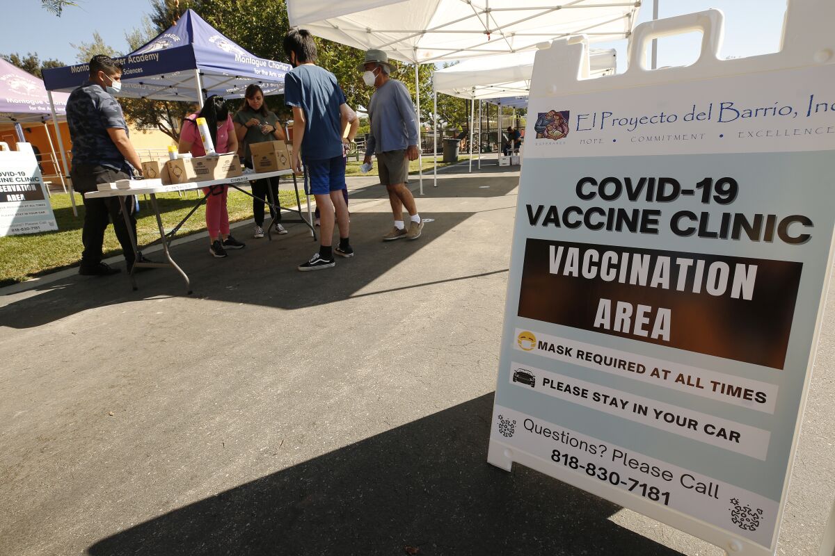 People in masks stand around a table next to a sign that says, in part, "COVID-19 vaccine clinic: Vaccination area."