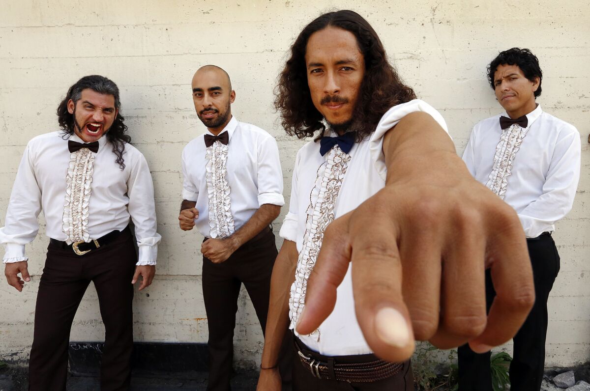 The four band members of Chicano Batman are shown in frilly tuxedo shirts before a white brick wall