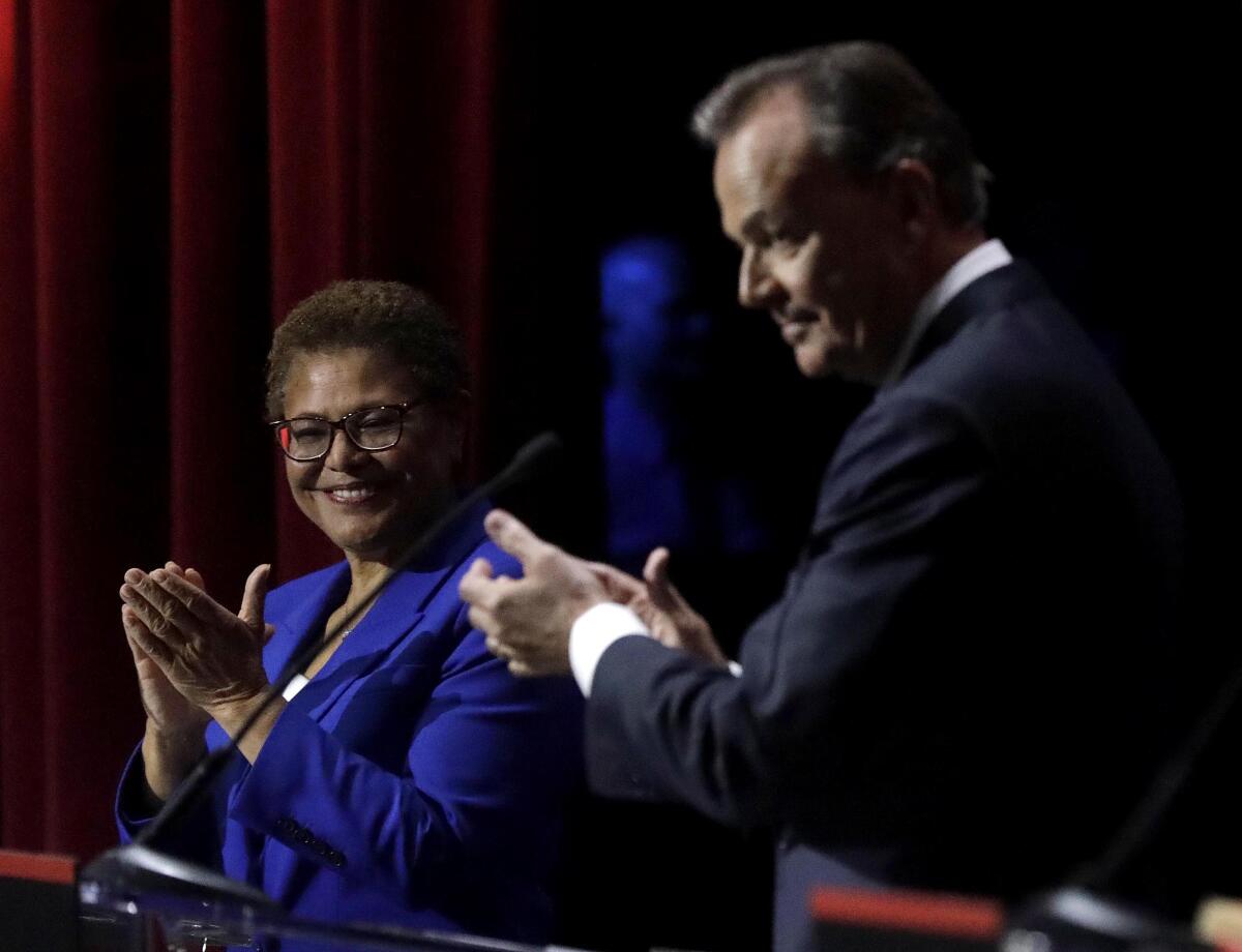 Two people standing at lecterns on a stage smile and applaud.