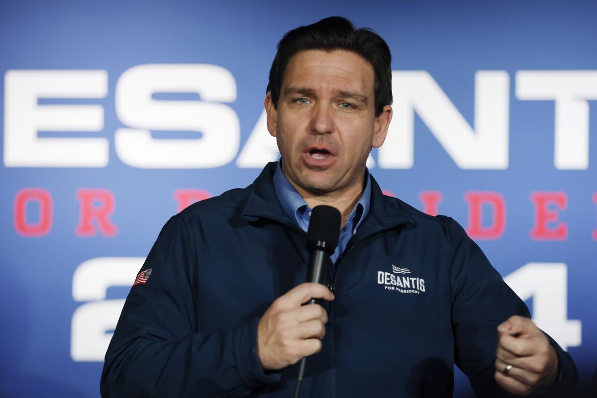 A man speaking into a mic in front of a sign that can be partially read (DeSantis for president 2024) 